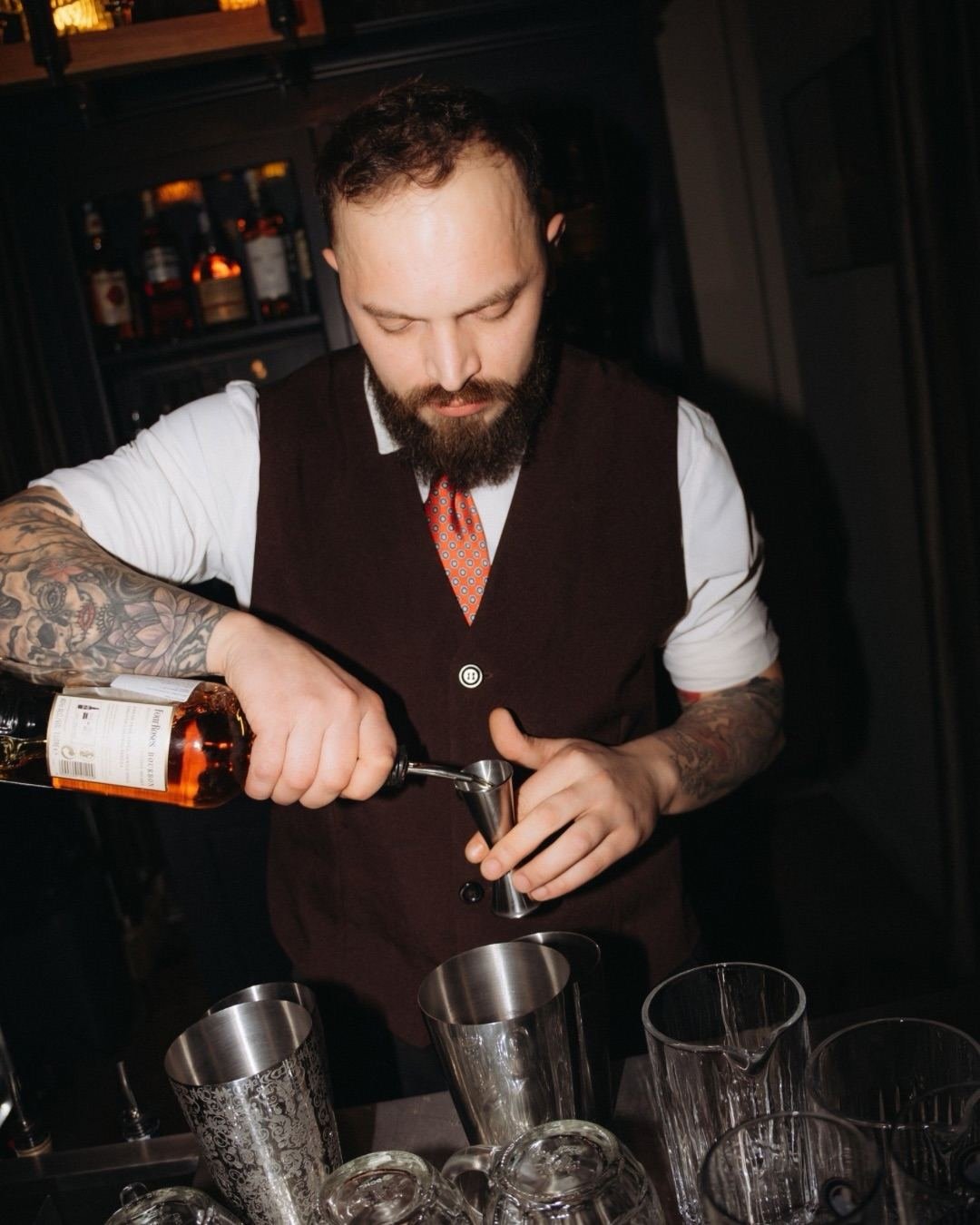 Bartender in a dark waistcoat pouring bourbon into a jigger