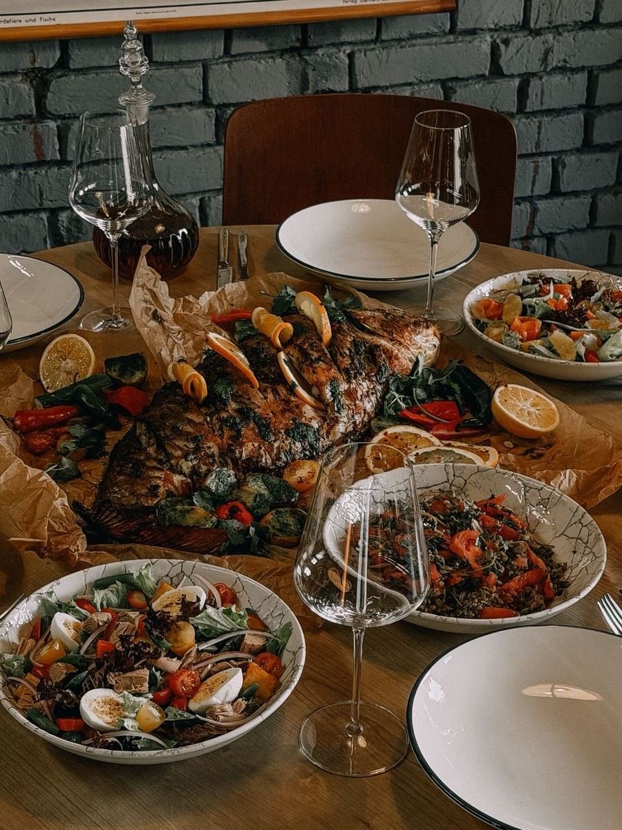 A whole grilled fish feast laid across the table with salads and wine