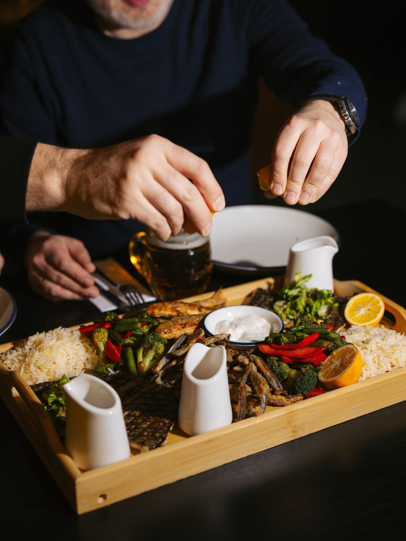 A wooden tray of fried smelt, grilled fish and rice being shared